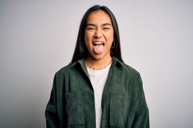 Genç, güzel Asyalı bir kadın, günlük gömleğini giyip izole edilmiş beyaz arka planda dikiliyor ve komik bir ifadeyle dilini dışarı çıkarıyor. Duygu kavramı.