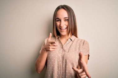 İzole edilmiş beyaz arka plan üzerinde dikilmiş, mutlu ve komik yüzlü genç ve güzel bir kadın. İyi enerji ve titreşimler.