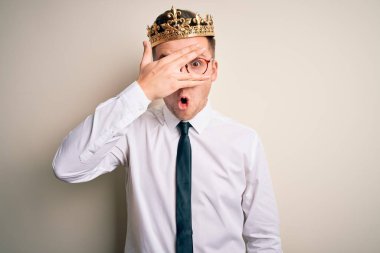 Kafkasyalı yakışıklı iş adamı, izole edilmiş arka planda altın taç takıyor. Şok olmuş bir şekilde yüzünü ve gözlerini kapıyor. Utanmış bir ifadeyle parmaklarından bakıyor..