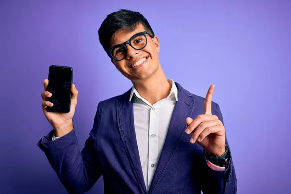 Mladý Pohledný Obchodník Bundě Brýlích Držící Smartphone Ukazující Obrazovku Překvapený — Stock fotografie