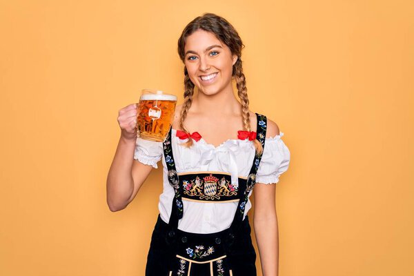Beautiful blonde german woman with blue eyes wearing octoberfest dress drinking jar of beer with a happy face standing and smiling with a confident smile showing teeth