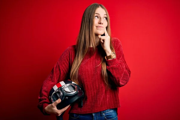 若い美しい赤毛の元ヘルメットを保持する元のオートバイの女性赤い背景深刻な顔を考えて質問については 非常に混乱したアイデア — ストック写真
