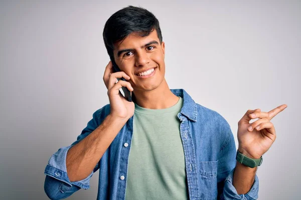 年轻英俊的男人在智能手机上用白色的背景交谈 他非常高兴地将手指和手指头指向旁边 — 图库照片