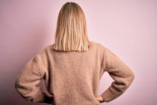 年轻美丽的金发女人 穿着冬季羊毛毛衣 披着粉色的孤立的背景 背对着身体 向后看去 — 图库照片