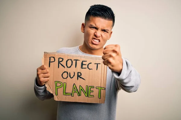 Young handsome activist latin man holding banner asking to protect our planet annoyed and frustrated shouting with anger, crazy and yelling with raised hand, anger concept
