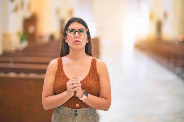 Young beautiful woman standing with hands together praying at church