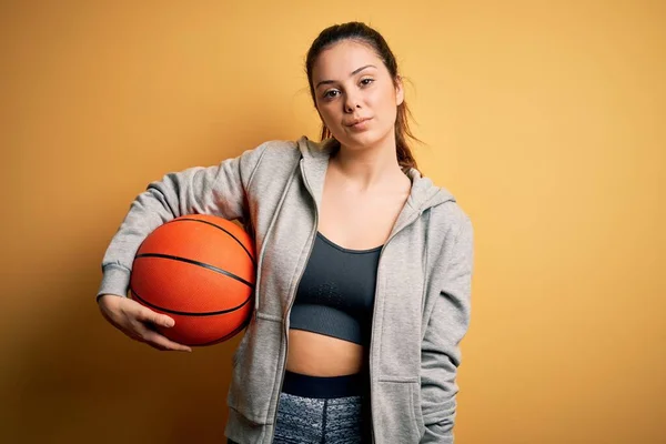 若いです美しいですブルネットスポーツ女性保持バスケットボールボール上の黄色の背景とともに自信を持って式上のスマート顔考え深刻な — ストック写真