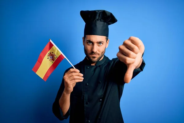 Mladý Pohledný Kuchař Plnovousem Uniformě Držící Španělskou Vlajku Rozhněvaným Obličejem — Stock fotografie