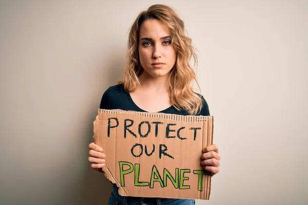 Young activist woman asking for environment holding banner with protect planet message with a confident expression on smart face thinking serious