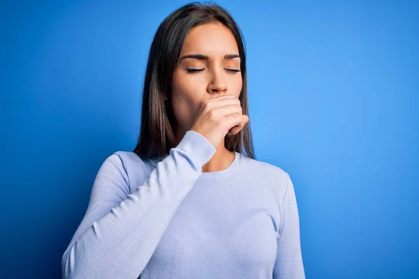 年轻美丽的黑发女人穿着宽松的毛衣站在蓝色的背景上 感觉不舒服 咳嗽是感冒或支气管炎的症状 保健概念 — 图库照片