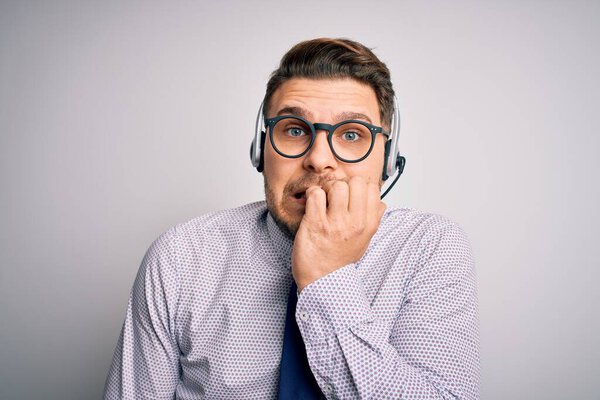 Young call center operator business man with blue eyes wearing glasses and headset looking stressed and nervous with hands on mouth biting nails. Anxiety problem.