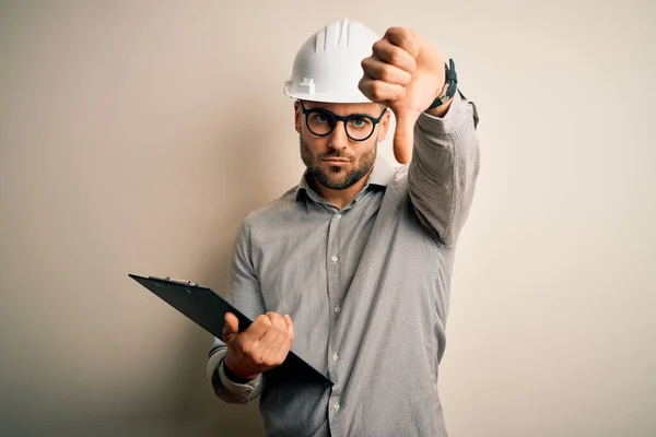 年轻的建筑师检查员头戴建筑工地安全帽 使用带有愤怒面孔的剪贴板 负面标志显示不喜欢戴大拇指 拒绝的概念 — 图库照片