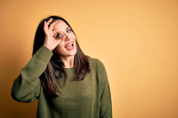 年轻的黑发女人 蓝眼睛 身穿绿色休闲衫 背景是黄色的 手握微笑 眼神流露在手指间 面带笑容 — 图库照片