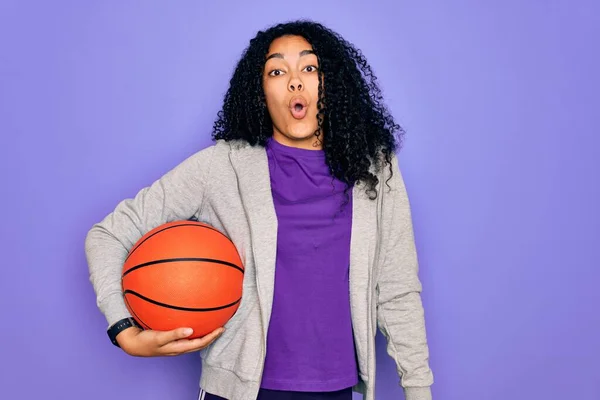 アフリカ系アメリカ人の女性は 驚きの顔でショックで怖がって紫色の背景の上にバスケットボールボールを保持スポーツをやって恐怖の表現で恐れと興奮 — ストック写真