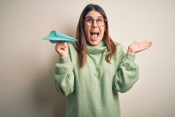 stock image Young beautiful woman holding airplane of paper standing over isolated grey background very happy and excited, winner expression celebrating victory screaming with big smile and raised hands