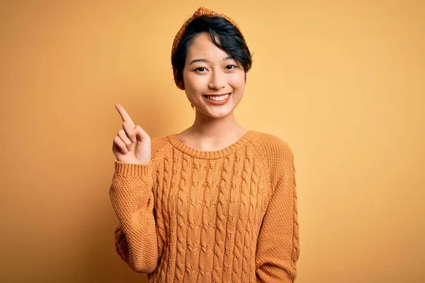 若い美しいアジアの女の子が成功したアイデアで指を指す黄色の背景の上に立ってカジュアルなセーターとダイエムを着ています 興奮し 第一番 — ストック写真