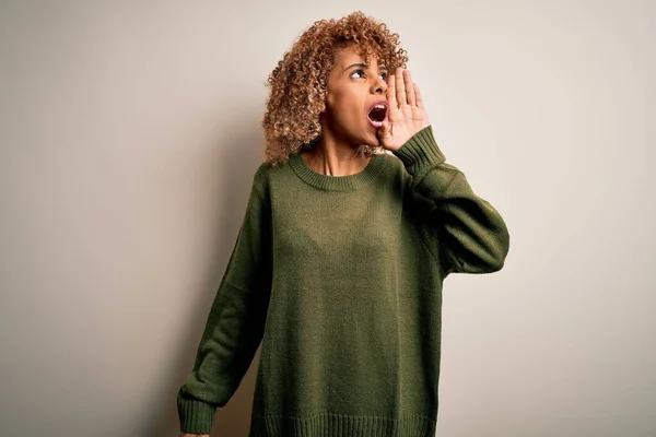 白い背景の叫びの上にカジュアルなセーターを着て巻き毛を持つ美しいアフリカ系アメリカ人女性と口の上に手で横に大声で叫んでいる コミュニケーションの概念 — ストック写真