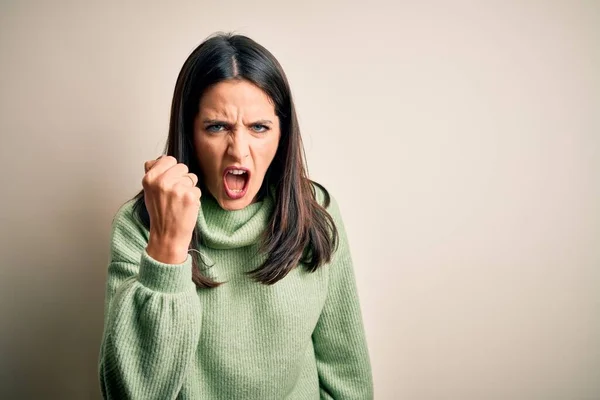白い背景の上にタートルネックセーターを着て青い目の若いブルネットの女性は怒りで叫んでいる間に怒りと怒りに苛まれ 激怒拳を上げ怒っている 激怒と積極的な概念 — ストック写真