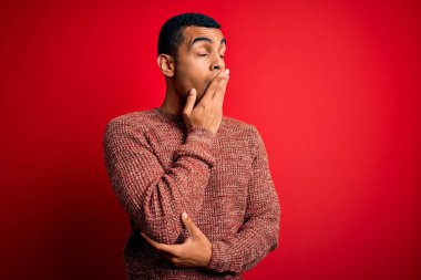 Genç, yakışıklı, Afro-Amerikan bir adam kırmızı arka planda dikilen günlük süveter giymiş, esnemekten sıkılmış, ağzı eliyle kapatmaktan sıkılmış. Huzursuz ve uykulu..