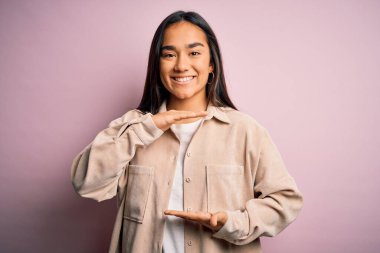 Genç, güzel Asyalı bir kadın pembe arka plan üzerinde dikilmiş büyük ve büyük boyut işareti ve ölçü sembolü gösteren el hareketleriyle günlük gömlekler giyiyor. Kameraya bakıp gülümsüyor. Ölçüm konsepti.