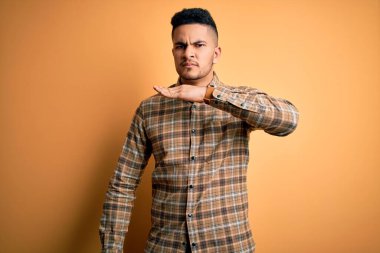 Sarı arka planda dikilip boğazını bıçak niyetine kesen genç ve yakışıklı bir adam öfkeli bir şiddetle saldırganlığı tehdit ediyor.