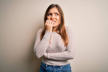 Güzel bir genç kadın, izole edilmiş bir arka planda, gergin ve gergin bir şekilde, elleri ağızdan tırnak yerken dikiliyor. Endişe sorunu.