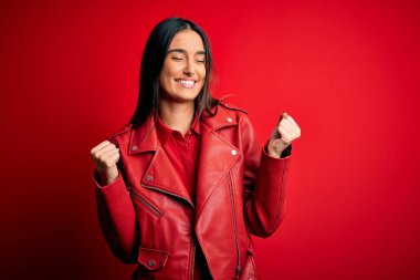 Genç, güzel esmer bir kadın, tek başına kırmızı arka planda dikilmiş mutlu ve heyecanlı bir şekilde kollarını kaldırarak, gülümseyerek ve başarı çığlıkları atarak zafer hareketi yapıyor. Kutlama konsepti.