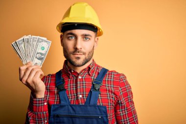 Güvenlik kaskı takan genç müteahhit sarı arka planda dolar karşılığı para tutuyor. Akıllı bir yüz ifadesiyle ciddi ciddi düşünüyor.