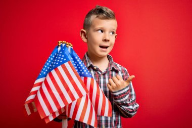 Amerika 'nın beyaz bayrağını kırmızı arka planda tutan ve gülümseyen küçük Amerikalı vatansever çocuk.