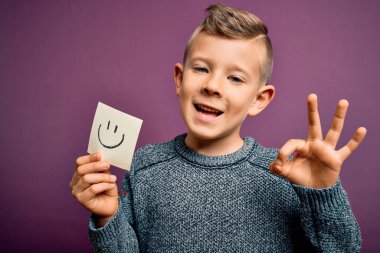 Küçük beyaz bir çocuk kağıtta gülen surat göstererek mutlu bir mesaj veriyor. Parmaklarıyla imza atıyor. Mükemmel bir sembol.