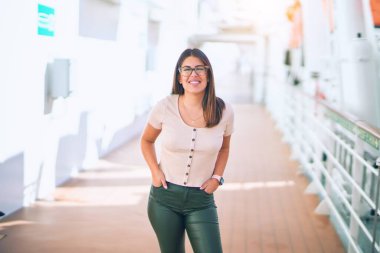 Tatilde mutlu ve kendinden emin gülümseyen genç ve güzel bir kadın. Yüzünde gülümsemeyle bir gemi güvertesinde durmak.