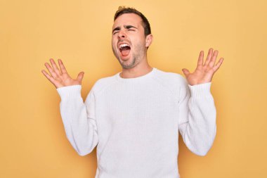 Mavi gözlü genç adam sarı arka planda dikilmiş çılgın ve çılgın başarısını kutluyor kolları havada ve gözleri kapalı heyecanla bağırıyor. Kazanan konsept