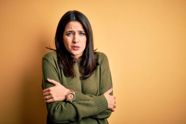 Mavi gözlü genç esmer kadın sarı arka planda yeşil bir süveter giyiyor. Soğuk yüzünden titriyor ve donuyor. Yüzünde üzgün ve şok ifadesi var.