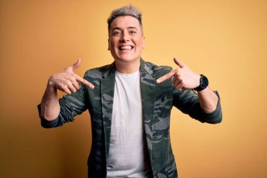 Sarı arka plan üzerinde duran yakışıklı, modern bir adam yüzünde bir gülümsemeyle gururla ve mutlu bir şekilde kendini işaret ediyor..