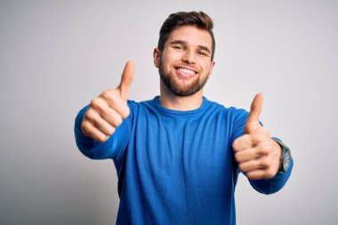 Sakallı, mavi gözlü, genç, yakışıklı, hoş bir sarışın, sıradan bir süveter giyiyor. Elle olumlu bir jest yapıyor, gülümsüyor ve başarı için seviniyor. Kazanan jest.