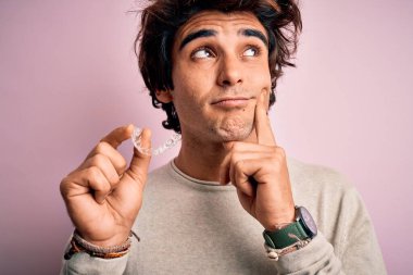 Genç yakışıklı bir adam pembe arka planda dikiliyor. Ciddi bir yüz. Soru soruyor, kafası karışık bir fikir.