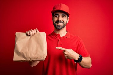 Sakallı genç, yakışıklı teslimatçı elinde yemek torbası, elinde de el ve parmak ile mutlu mesut işaret ediyor.