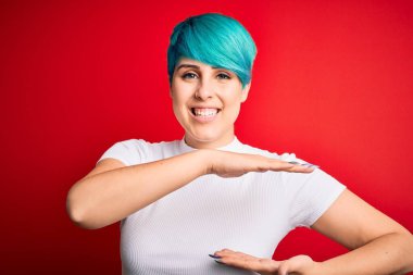 Mavi saçlı, kırmızı arka planda sıradan tişörtler giyen, büyük ve büyük beden işaretleri gösteren genç ve güzel bir kadın. Kameraya bakıp gülümsüyor. Ölçüm konsepti.