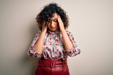 Genç ve güzel kıvırcık Arap kadın çiçek tişörtü giyerek izole edilmiş beyaz arka planda dikiliyor. Başı ağrıyor çünkü stres altında. Migren ağrısı..
