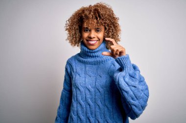 Güzel Afro-Amerikan kadın balıkçı yaka kazak giyip beyaz arka planda gülümsüyor ve el hareketleriyle küçük beden işareti yaparak kameraya bakıyor. Ölçü kavramı.