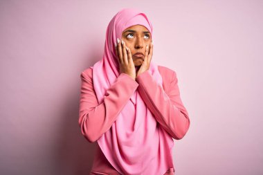 Genç Afrikalı Afro kadın pembe arka plan üzerine Müslüman başörtüsü takıyor. Yüzü, depresyonu ve üzüntüyü örten eller, sorun yüzünden üzgün ve tedirgin.