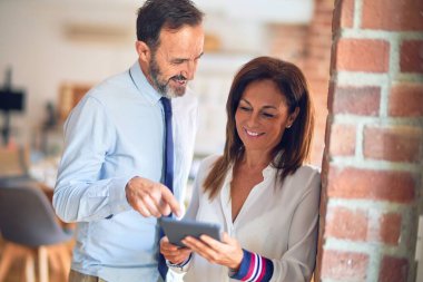 Mutlu ve kendinden emin gülümseyen iki orta yaşlı iş adamı. Ofiste tablet kullanarak birlikte çalışmak, gülümsemek.