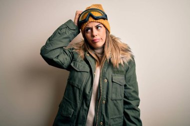 Genç esmer kayakçı kadın kar giysileri ve kayak gözlüğü takıyor beyaz arka plan karışıklığı ve soru sormayı merak ediyor. Şüpheyle kararsız, kafa kafaya düşünerek. Düşünceli kavram.