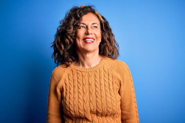 Orta yaşlı, güzel bir kadın izole edilmiş sarı arka plan üzerine sıradan sarı süveter giyiyor. Yüzünde gülümseme, doğal bir ifade ile yan yana bakıyor. Kendinden emin gülen.