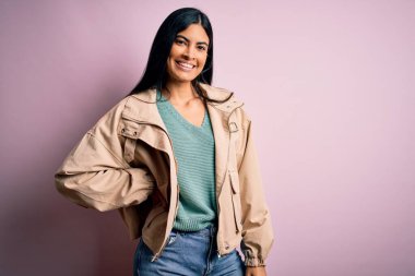 Moda kıyafetleri giyen genç ve güzel bir kadın. Manken, sokak tarzı giyiniyor. Pembe arka planda dikiliyor.