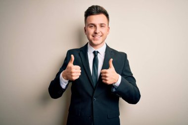 Zarif takım elbiseli ve kravatlı genç yakışıklı iş adamı izole edilmiş arka plan başarı tabelasına el hareketleriyle olumlu jest yapıyor, gülümsüyor ve mutlu. Neşeli ifade ve kazanan jest.