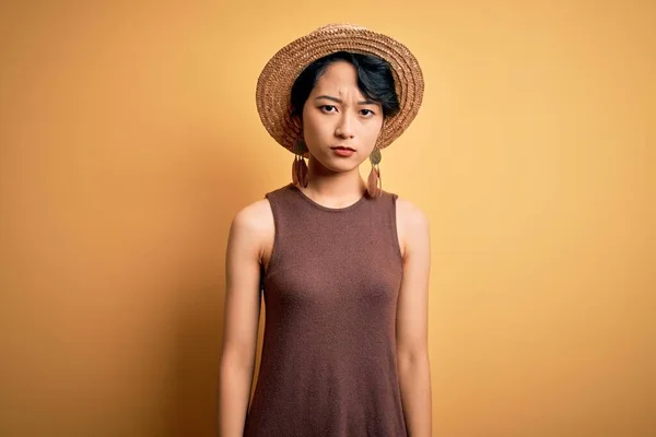若い美しいアジアの女の子のカジュアルTシャツを着て 帽子の上に孤立した黄色の背景懐疑的で緊張し 問題のために動揺を眉をひそめて 負の人 — ストック写真