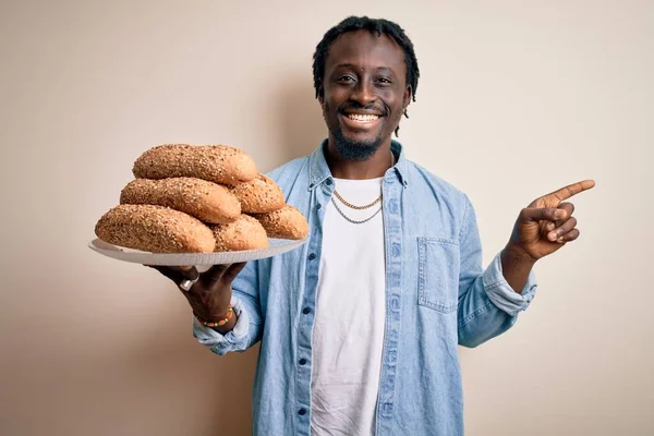 年轻的非洲裔美国人拿着一个盘子 盘子里有健康的全麦面包 背景是白色的 他非常高兴地将手和手指指向旁边 — 图库照片