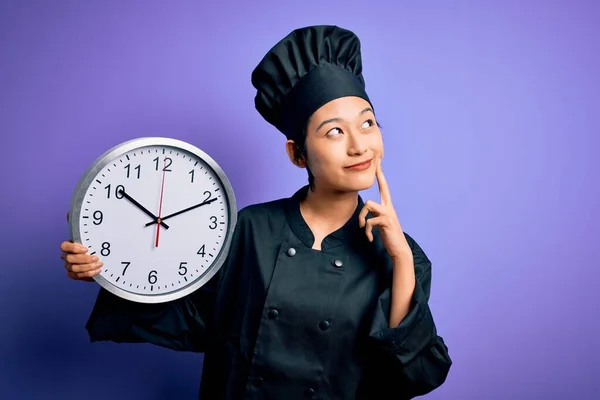 中国女厨师身穿炊具制服 头戴帽子 头戴倒计时钟 满脸严肃地思考着问题 非常迷惑的想法 — 图库照片