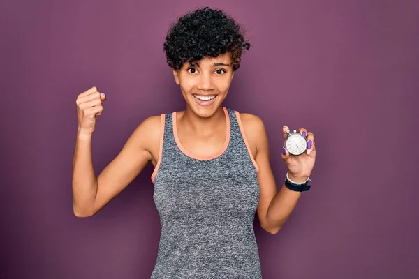 年轻美丽的非洲裔美国女运动员 手握秒表 身披紫色背景 自豪地尖叫着 庆祝胜利和成功 非常兴奋 欢呼着感情 — 图库照片